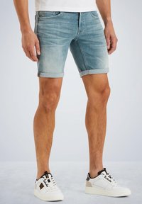 Pantalones cortos de mezclilla en azul claro con dobladillos enrollados, que cuentan con bolsillos frontales, cremallera y un acabado desgastado para un look casual. Combinados con zapatillas blancas.