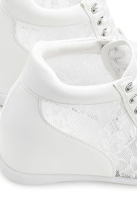 Weiße Sneaker mit Schnü rungsbändern, abgerundeter Zehenpartie, silbernen Ösen und gepolstertem Schaft. Glattes Leder und zarte Spitze bilden einen Kontrast.