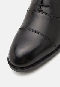 Pantofii de dress din piele neagră prezintă un finisaj neted, bot rotund, cusături decorative și o talpă din cauciuc texturat.