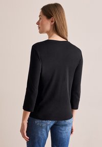 Schwarzes Langarmoberteil mit Rundhalsausschnitt, glatter Textur und 3/4-Ärmeln, kombiniert mit blauen Jeans.