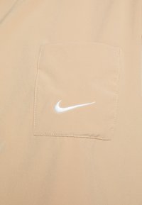 Beige tygficka med vit Nike swoosh-logotyp sydd i mitten.