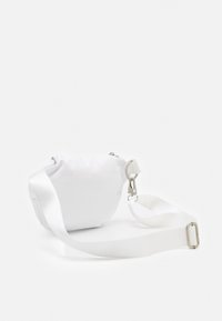 Mała biała tkaninowa torebka na ramię z regulowanym paskiem i srebrnym metalowym zapięciem na białym tle.