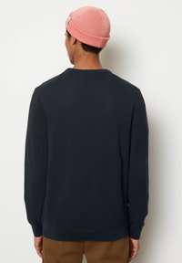 Marineblauer Strickpullover mit rundem Halsausschnitt und gerippten Bündchen, kombiniert mit einer hellrosa gerippten Mütze. Das Material wirkt strukturiert.