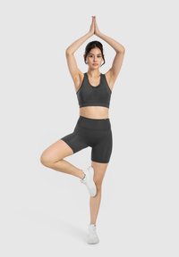 Set di top corto e pantaloni sportivi neri. Il tessuto presenta una texture liscia. Il modello è in posa su una gamba con le braccia sollevate.