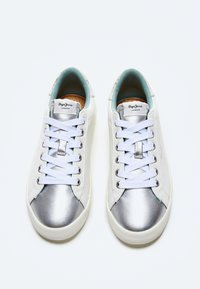Zapatillas blancas con puntera metálica plateada, forro interior celeste y cordones blancos; presentan un diseño minimalista y suela de goma texturizada.