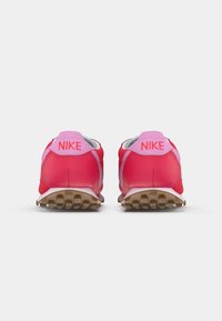 Par de sapatilhas Nike vermelhas e cor-de-rosa vistas por trás, com solas texturizadas e o logótipo da Nike na aba do calcanhar.