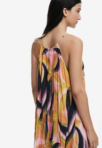 Abito vivace senza maniche con un design fluido, caratterizzato da motivi floreali multicolori in rosa, arancione e nero. Tessuto leggero e testurizzato.