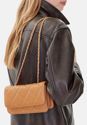 Frau trägt schwarze Lederjacke und eine hellbraune gesteppte Umhängetasche mit goldener Kettenriemen über der Schulter