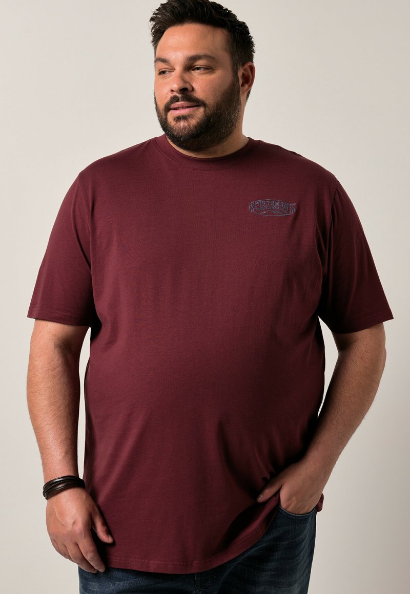 T-shirt rouge bordeaux à manches courtes en coton, avec un petit logo graphique bleu sur la poitrine et une coupe décontractée. Style décontracté avec texture.