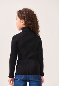 Melnās ribotās adītas turtlenecka džemperis ar garām piedurknēm, pieguļoša forma un tekstūrēts raksts, saskaņots ar ziliem džinsiem.
