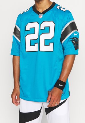 Homme portant un maillot bleu des Carolina Panthers NFL numéro 22 avec un short rayé noir et blanc et un bracelet Nike noir.