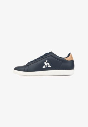 Sneaker blu navy a taglio basso con suola bianca, chiusura con lacci, linguetta del tallone color cuoio e logo bianco stilizzato di un uccello sul lato.
