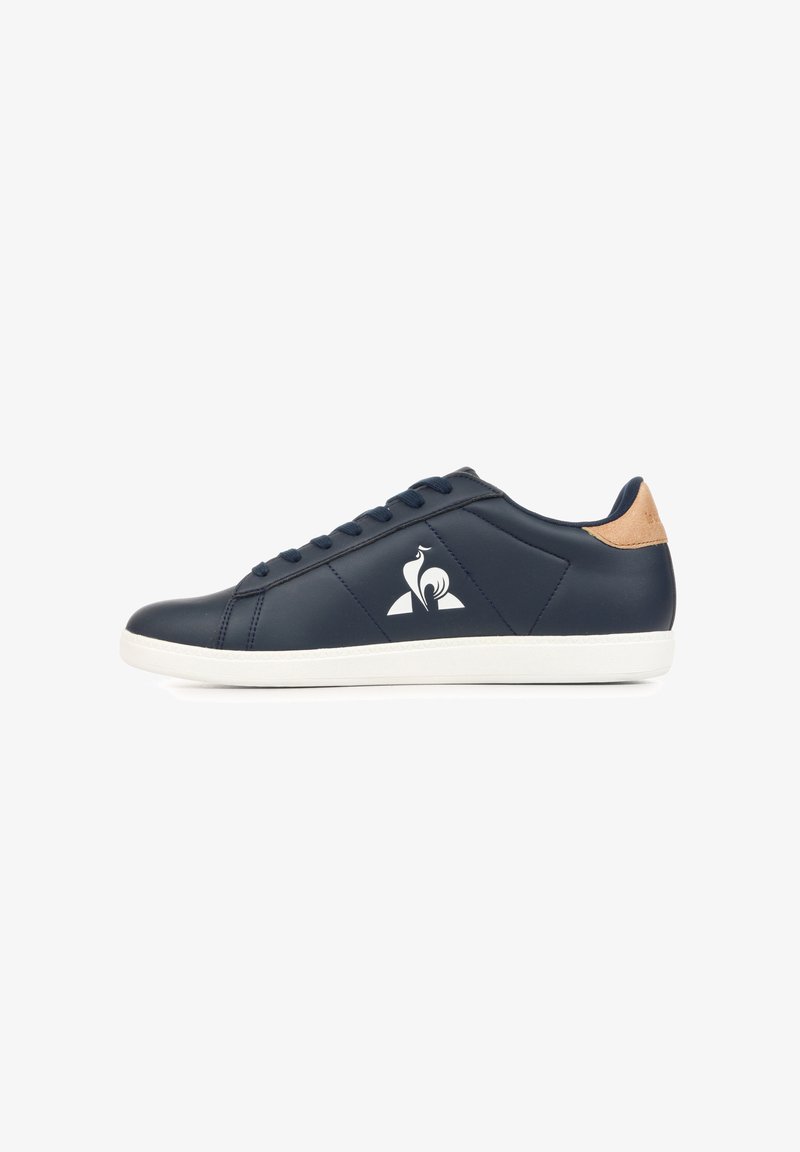 Sneaker blu navy a taglio basso con suola bianca, chiusura con lacci, linguetta del tallone color cuoio e logo bianco stilizzato di un uccello sul lato.
