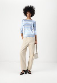 Ριγέ μακρυμάνικο μπλουζάκι σε ανοιχτό μπλε και λευκό, σε συνδυασμό με κρέμ παντελόνι με φαρδιά πόδια. Διαθέτει μικρό λογότυπο και μαύρες ψηλές σαγιονάρες.