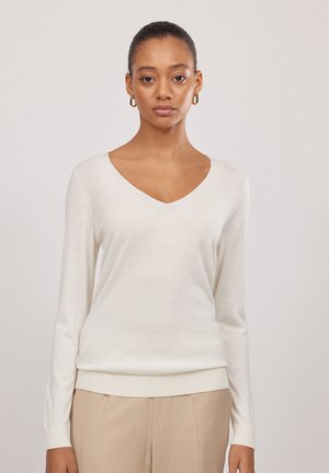 Weißer Pullover mit langen Ärmeln und V-Ausschnitt, aus einem weichen Material. Verfügt über gerippte Bündchen und Saum. Kombiniert mit beigen Hosen.