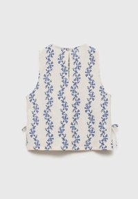 Top sans manches en tissu léger avec des motifs floraux verticaux bleus sur un fond crème ; présente des fermetures à nouer sur les côtés et un bouton au dos.