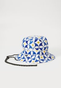 Blå og hvid bucket hat med geometriske mønstre, der har gule accenter, justerbar sort snor og et syet mærke på siden.