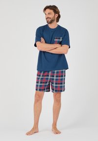 Conjunto de ropa de estar para hombres; camiseta de manga corta en navy con un bolsillo de cuadros, combinada con pantalones cortos de cuadros en rojo, azul y blanco. Material de algodón, corte relajado.