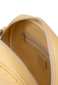 Interno di una borsa in pelle gialla con una texture liscia, dotata di una piccola tasca con zip e un'etichetta con il logo. Non foderato con una finitura morbida.