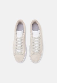 Baskets en daim beige avec une semelle en caoutchouc blanche, dotées d'une semelle intérieure texturée bleu clair et de lacets gris, conçues pour un usage décontracté.