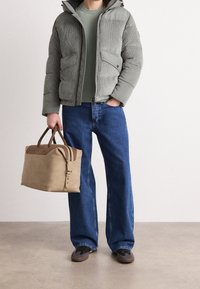 Szara pikowana kurtka ze sztruksu z kapturem, zielony sweter, szerokie niebieskie dżinsy oraz beżowa torba typu duffel z brązowymi skórzanymi akcentami. Ciemne buty.