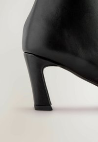 Sort højhælet sko med en struktureret læderoverdel, et forlænget design og en robust, smal hæl med en let udsparing bagpå.