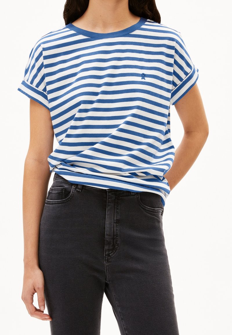 Personne portant une chemise à manches courtes rayée bleu et blanc horizontal, rentrée dans un jean noir taille haute.