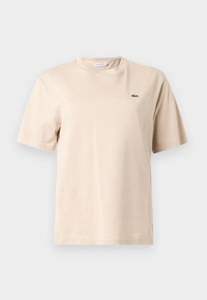 Camiseta de algodón beige con cuello redondo, mangas cortas y un pequeño logo de cocodrilo verde bordado en el pecho izquierdo.