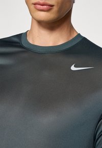 Nike pikkade varrukatega performance t-särk tumesinises värvitoonis, millel on sile tekstuur, ümar kaelus ja diskreetne peegeldav logo rinnal.