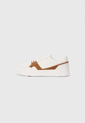 White sneaker with brown suede accents, featuring a textured finish, round toe, thick sole, and traditional lace-up design.