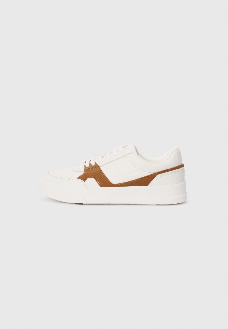 White sneaker with brown suede accents, featuring a textured finish, round toe, thick sole, and traditional lace-up design.
