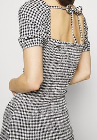 Robe à carreaux noir et blanc avec manches courtes bouffantes et dos nu, dotée d'une fermeture à nœud papillon et d'un tissu froncé pour la texture.