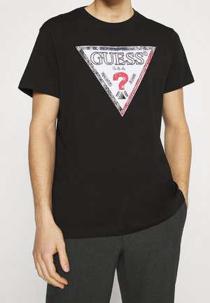 Black cotton t-shirt featuring a large triangular graphic with the "GUESS" logo and red accents, and bold question mark design in the center.