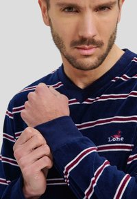 Camisa de manga larga a rayas marino. Presenta rayas blancas y burdeos, diseño de cuello en V y un logo bordado en el pecho. Textura suave.