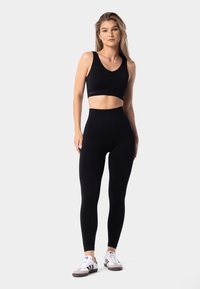 Top corto atlético negro y leggings de cintura alta, ambos con una textura suave. Modelo lleva zapatillas blancas y grises. Diseño sencillo y moderno.