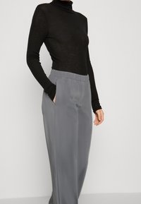 Un haut à col roulé noir associé à un pantalon taille haute lisse gris clair avec des poches latérales et une taille élastique.