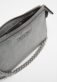 Metaliczna szara skórzana kopertówka o fakturowanym wykończeniu, z zamkiem błyskawicznym i srebrnym łańcuszkiem. Posiada wytłoczone logo z przodu.