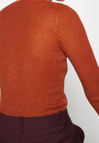 Geribbelde, getailleerde trui in fel oranje met een subtiele glans, met lange mouwen en een ronde halslijn, gecombineerd met donkerpaarse broeken.