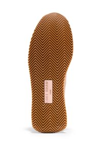Gummisko med zigzag-mönster på sulan, ljusbrun färg, märkt med "Cole Haan 1928" i en rektangulär accent.