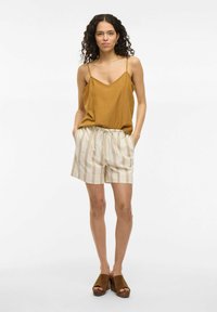 Top de tirantes fino color marrón claro, combinado con pantalones cortos beige a rayas con cintura ajustable. Sandalias de plataforma marrones.