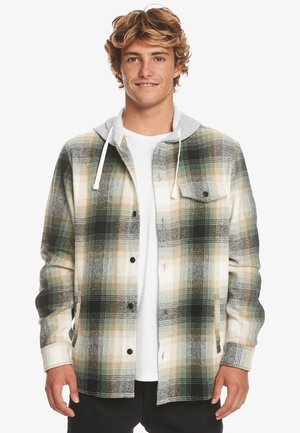 Rutig flannel skjorte i grønne, beige og sorte nuancer med en grå hætte trøje fastsyet. Har knaplukning foran og brystlomme. Blødt materiale.