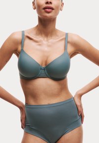 Sostenitore modellato in teal attenuato, con spalline regolabili, un accessorio centrale a fiocco e una mutandina alta coordinata con texture liscia.