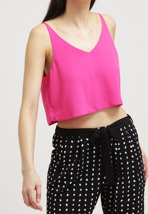 Kobieta ubrana w różowy krótki top bez rękawów i czarne spodnie z wysokim stanem w białe kropki, z wiązanym paskiem.