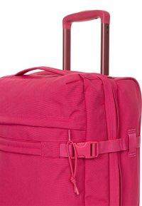 Valigia rosa brillante con tessuto strutturato, manico retrattile, tracolla laterale e dettaglio con tasca con cerniera. Materiale resistente con design funzionale.
