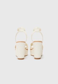 Sandales à plateforme blanches avec une texture tissée sur le talon, une bride de cheville réglable et un matériau supérieur lisse.