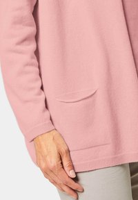 Hellrosa Strickjacke aus weichem Material, mit rundem Ausschnitt, gerippten Bündchen und einer kleinen aufgesetzten Tasche auf der Vorderseite.