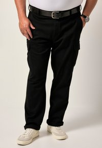 Pantaloni cargo neri con tasche laterali, realizzati in tessuto resistente, con una vestibilità ampia e orli arrotolati. Indossati con una cintura nera e sneakers bianche.