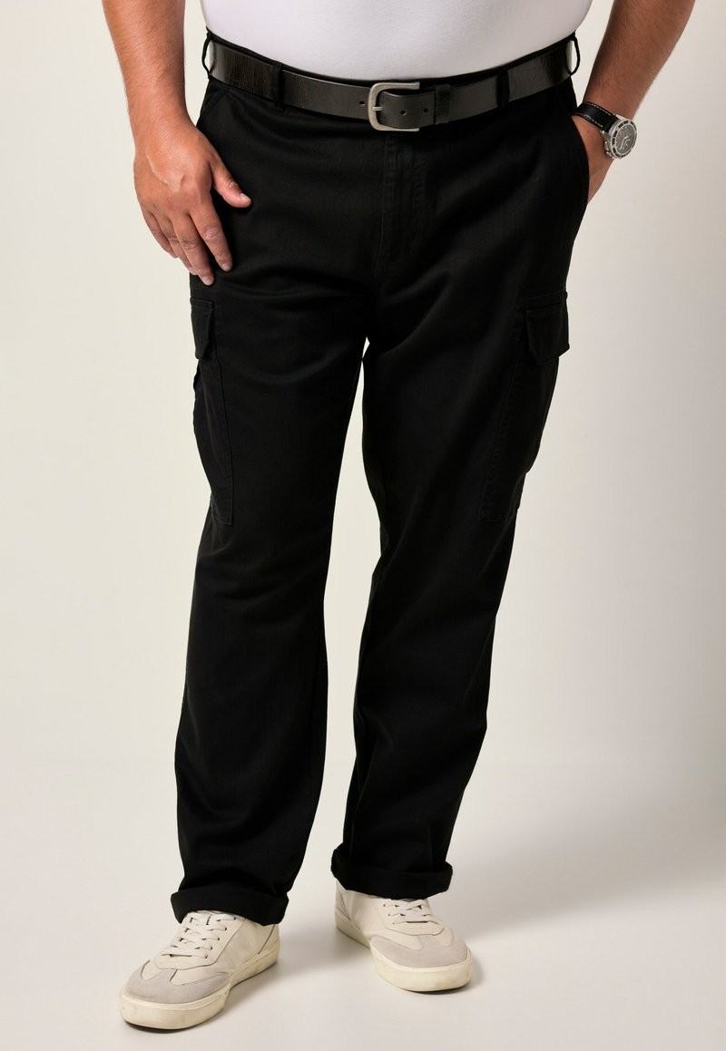 Pantaloni cargo neri con tasche laterali, realizzati in tessuto resistente, con una vestibilità ampia e orli arrotolati. Indossati con una cintura nera e sneakers bianche.