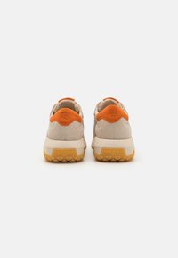 Beige semskinn-sneakers med oransje detaljer på hælen. Har en teksturert gummisåle med merkevarelogg og en polstret tunge for komfort.