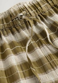 Groene geruite shorts met een zachte textuur, voorzien van een elastische tailleband en een trekkoorddetail. Strepen in beige en donkerbruin accenten.